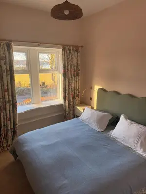 a bedroom with a blue bed with two pillows and a window at Skinnel Cottage in Kirkcudbright