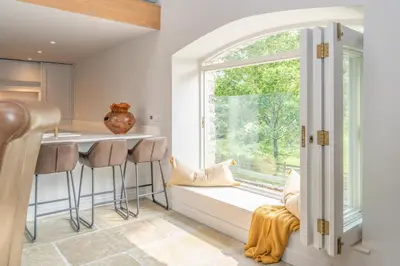 a kitchen with a window and a counter with stools at Luxurious Barn within easy reach of South Lakes! in Boot