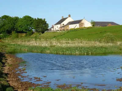 a house on top of a hill next to a pond at Stanegate, Irthington on Hadrians Wall in Irthington