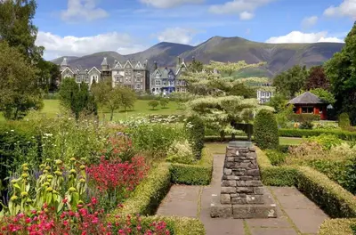 a garden in front of a large house with mountains in the background at Wordsworth Cottage in Keswick