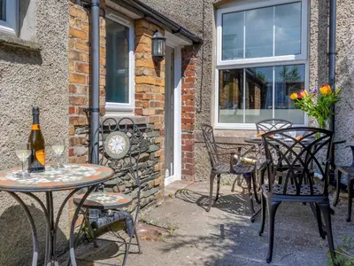 a patio with tables and chairs and a bottle of wine at Jame's Cottage in Keswick