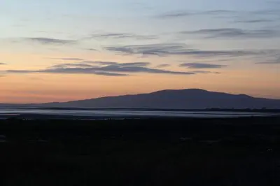 a sunset over the water with mountains in the background at Paws A While in Mainsriddle