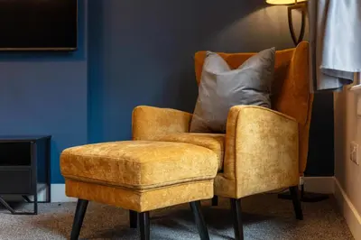a yellow chair with a pillow and a stool at No8 Peebles Retreat - Donnini Apartments in Ayr