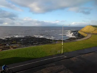 a person riding a bike on a road next to the ocean at Wood Court, Troon in Troon