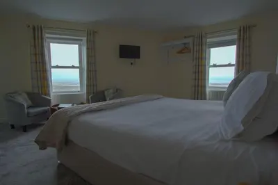 a bedroom with a bed and a chair and two windows at The Harbour Inn in Garlieston