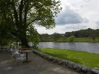 a picnic table and chairs next to a river at The Ken Bridge Hotel & Campsite in New Galloway
