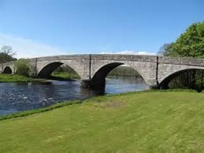 a stone bridge over a river with a grass field at The Ken Bridge Hotel & Campsite in New Galloway