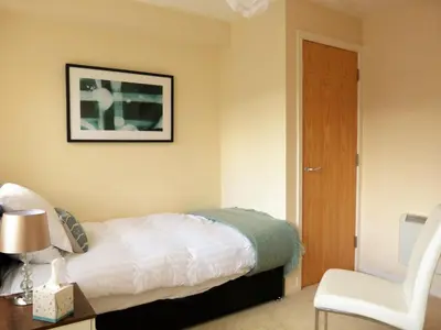 a bedroom with a bed and a white chair at The Sawmills, Carlisle - Spacious 4 Bedroom Family House - Free WiFi - & Parking - Walk to Carlisle Castle in Carlisle