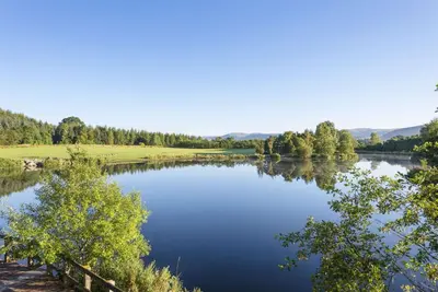 a view of a lake with trees and mountains in the background at Days Inn Lockerbie - Annandale Water in Johnstonebridge