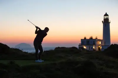 a man playing golf with a lighthouse in the background at Trump Turnberry in Turnberry