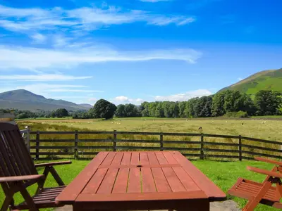 a wooden picnic table with two chairs and a field at Blencathra in Mungrisdale