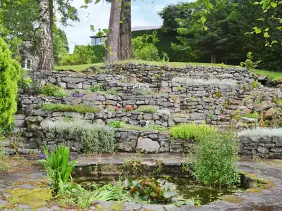 a stone wall with a pond in a garden at Dye Mill Cottage in Moffat