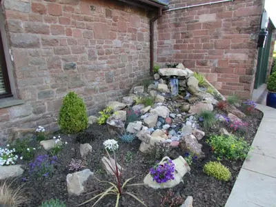 a garden with rocks and flowers in front of a brick wall at Fell View in Troutbeck