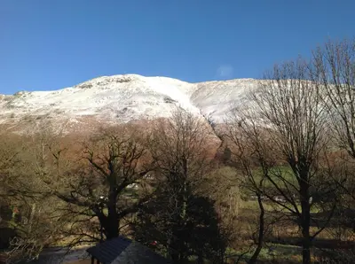 a snow covered mountain with trees in front of it at Old Water View in Patterdale