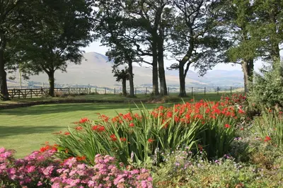 a garden with flowers and trees and mountains in the background at Grisdale View in Penrith