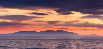 a sunset over the ocean with mountains in the background at The Original Donnini Apartment in Ayr