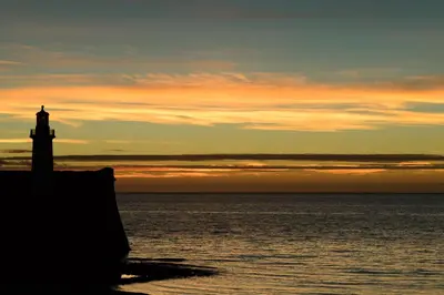 a lighthouse on the shore of the ocean at sunset at The Mansion in Whitehaven