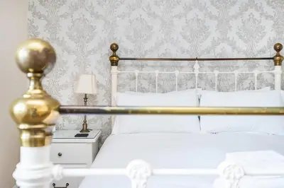 a bedroom with a white bed with a gold headboard at Cragwood Guest House in Keswick