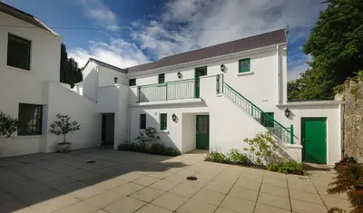 a white house with green doors and a courtyard at Milntown Self Catering Apartments in Ramsey