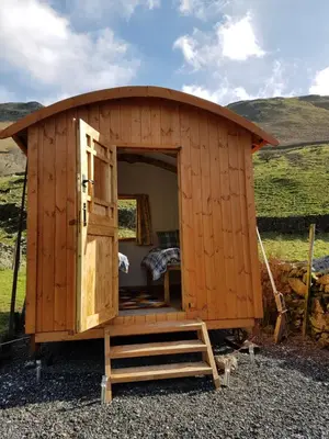 a wooden shed with a open door in a field at Stybeck Farm Shephards Hut in Thirlmere