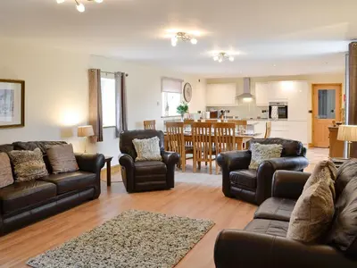 a living room with a couch and chairs and a kitchen at The Wheat Shed in Calthwaite