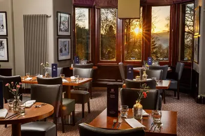 a restaurant with wooden tables and chairs and windows at Holiday Inn Dumfries by IHG in Dumfries