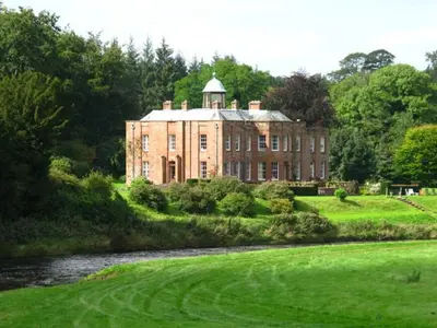 a large brick building with a tower on top of a field at Warwick Hall in Carlisle