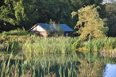an old cabin sits next to a body of water at Carnell Country Estate & Holiday Cottages in Ayrshire in Hurlford