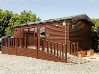 a cabin with a wooden fence and a porch at Green View Lodges in Wigton