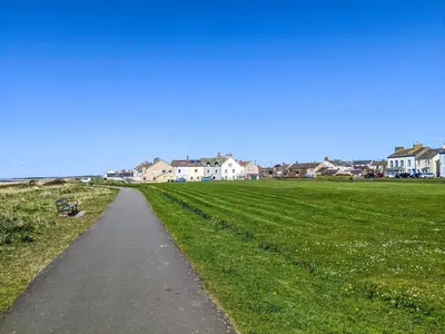 a path through a field with houses in the background at Cosy Cottage in Allonby