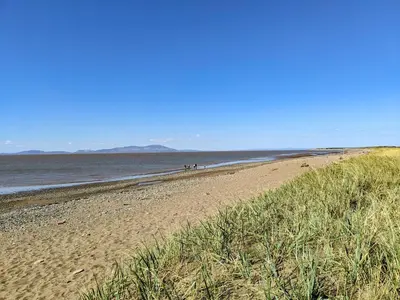 a beach with two people walking on the sand at Cosy Cottage in Allonby