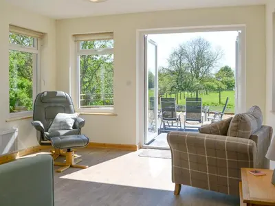a living room with a couch and chairs and a sliding glass door at Riverside Cottage in Boreland