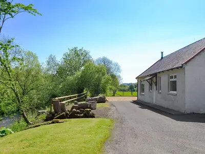 a building with a pile of logs next to a road at Riverside Cottage in Boreland