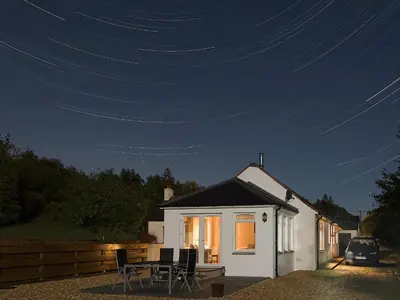 a small white house with a table and chairs at night at Riverside Cottage in Boreland