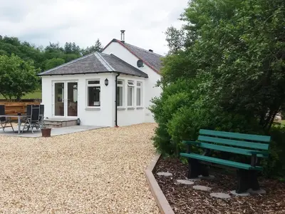 a white cottage with a green bench in front of it at Riverside Cottage in Boreland