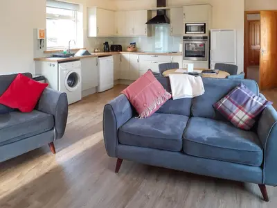 a living room with a blue couch and a kitchen at Riverside Cottage in Boreland