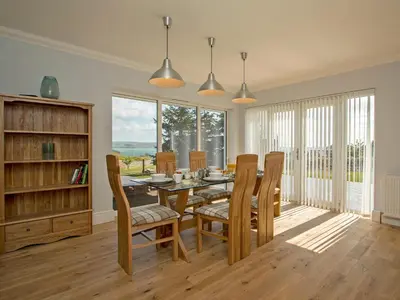a dining room with a table and chairs and windows at Quarter Acre House in Challoch