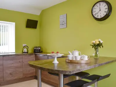 a kitchen with a table and a clock on the wall at Hameish Holiday Cottage in Kirkcudbright