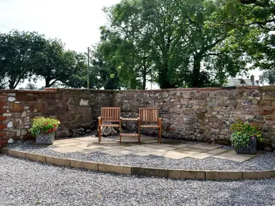 two chairs and a table in front of a stone wall at Bruno's Bothy in Wigton