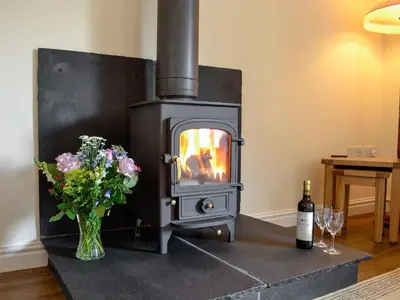 a wood stove with a vase of flowers and a bottle of wine at Bruno's Bothy in Wigton