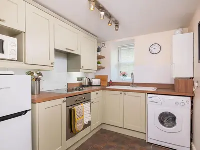 a kitchen with white cabinets and a washer and dryer at Bunbury Cottage in Keswick