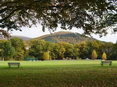 two benches in a park with a mountain in the background at 1 Greta Side Court in Keswick