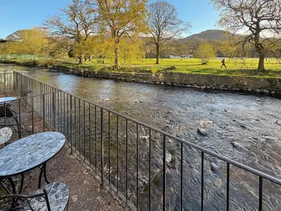 a river with a table and chairs next to a fence at 2 Greta Side Court in Keswick