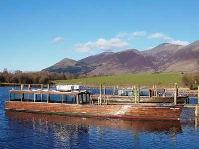 a boat is docked on the water with mountains in the background at Olivet - Hewetson Court in Keswick