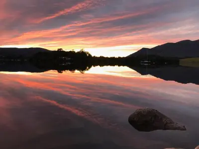 a sunset on a lake with a rock in the water at 3 Catherine Cottages in Keswick