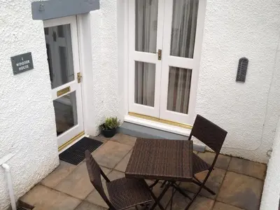 a patio with two chairs and a table and two windows at 1 Windsor House in Keswick