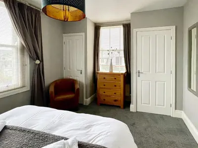 a bedroom with a bed and a chair and windows at High Style Apartment in Keswick