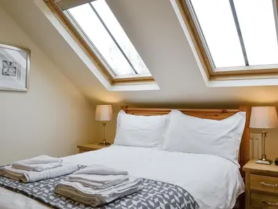 a bedroom with a bed with white sheets and two windows at The Old Laundry 4 in Keswick