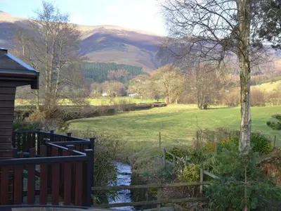 a house with a fence and a stream in a field at Glenmore Lodge in Keswick