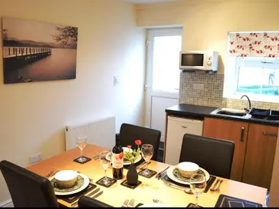 a dining room with a table with chairs and a kitchen at Uncle's Cottage in Keswick